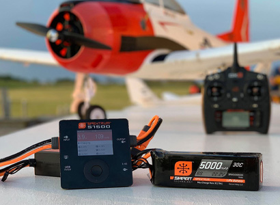 Picture of a RC plane and transmitter in the background featuring a Spektrum charger and battery.